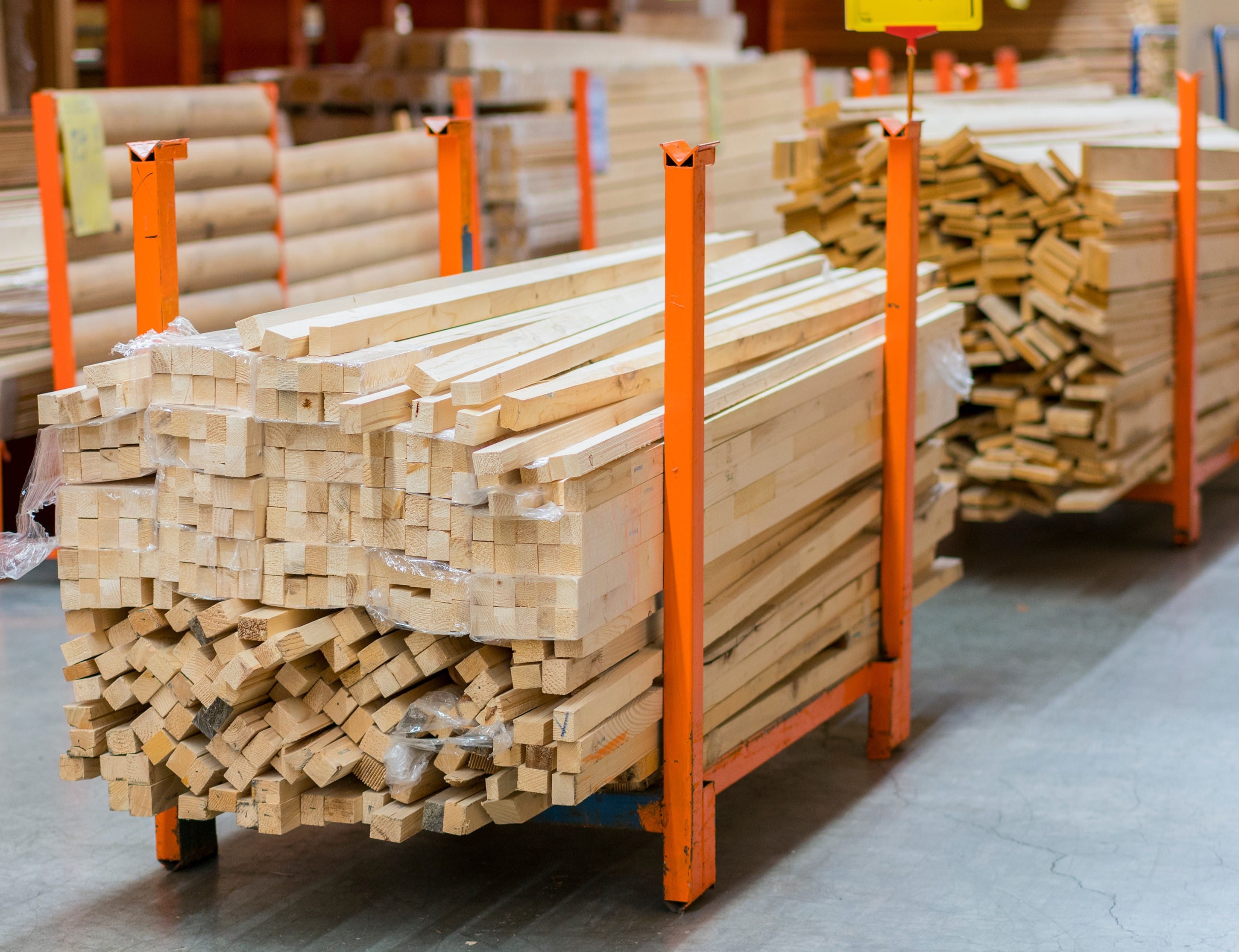 stack new wooden bars on shelves inside lumber yard of large hardware store in america. rack of fresh mill or cut wood timber with flatbed cart and manual forklift in warehouse.